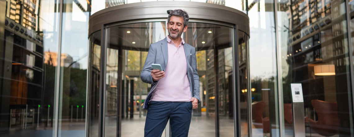 business-man-happily-surfing-phone-while-going-through-automatic-curved-sliding-door